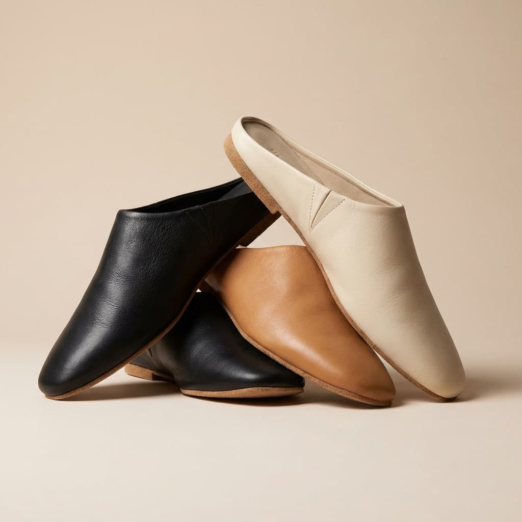 Set of minimal leather mules in black tan and cream arranged as a bundle on neutral background.
